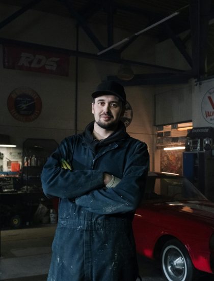 Bearded male mechanic standing confidently in a classic car garage.